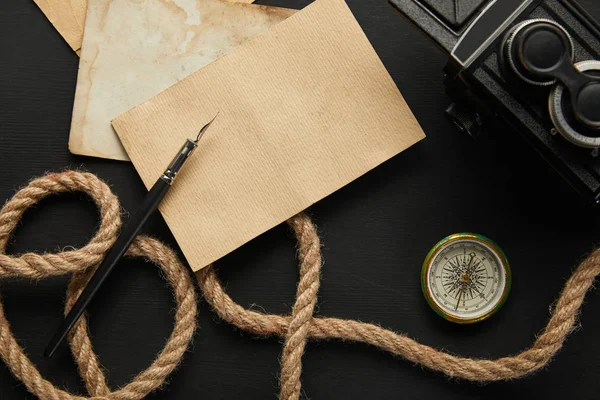 Vista dall'alto di fotocamera vintage, carta, corda, penna stilografica, bussola su sfondo nero — Foto stock