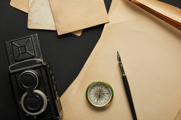 Vue du dessus de la caméra vintage, papier, stylo plume, boussole sur fond noir — Photo de stock