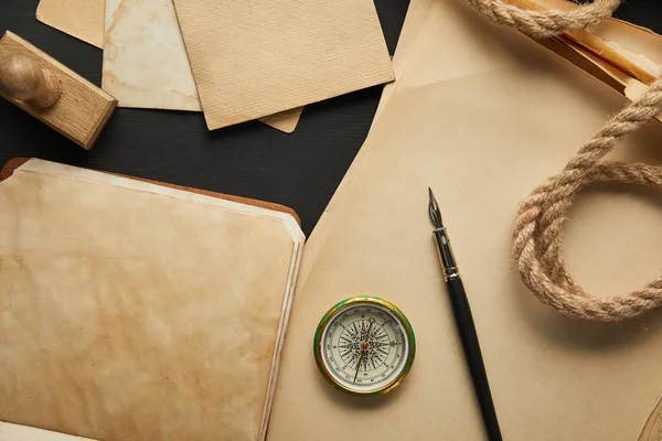 Vista dall'alto di carta vintage, corda, bussola, timbro e penna stilografica su sfondo nero — Foto stock