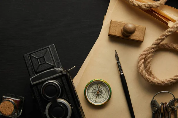 Vue de dessus de la caméra vintage, papier, stylo plume, boussole, timbre et clés sur fond noir — Photo de stock