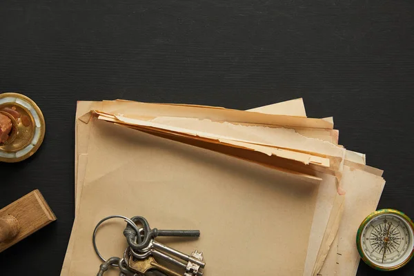 Vista superior de papel vintage, chaves, bússola e carimbo sobre fundo preto — Fotografia de Stock