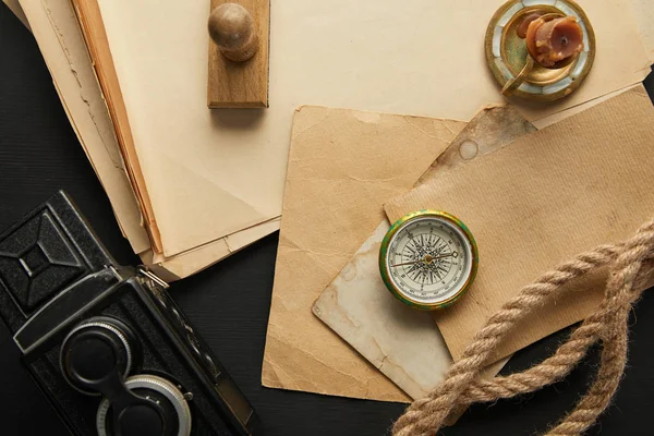 Vue de dessus de la caméra vintage, papier, corde, boussole, bougie et timbre sur fond noir — Photo de stock