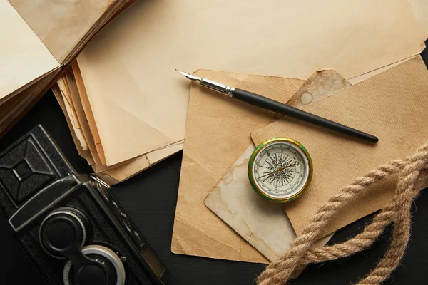 Vue de dessus de la caméra vintage, papier, corde, boussole et stylo plume sur fond noir — Photo de stock