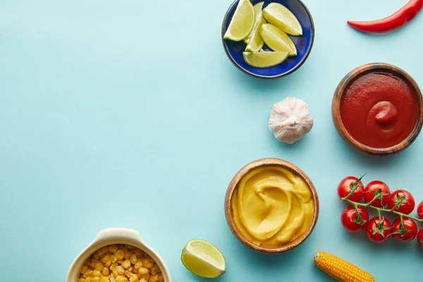 Vue du dessus de lime, moutarde à la sauce tomate et légumes sur fond bleu — Photo de stock