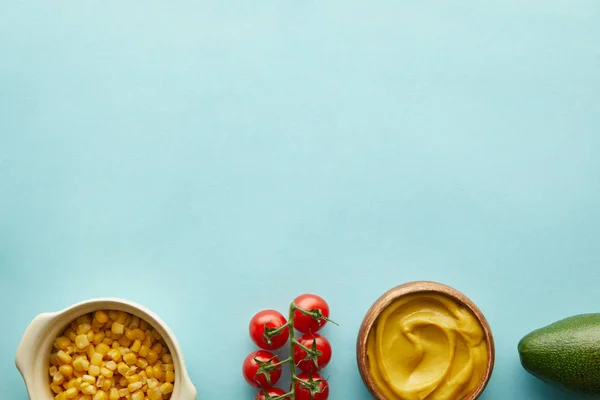 Vista dall'alto di mais, senape con avocado e pomodorini su sfondo blu con spazio copia — Foto stock