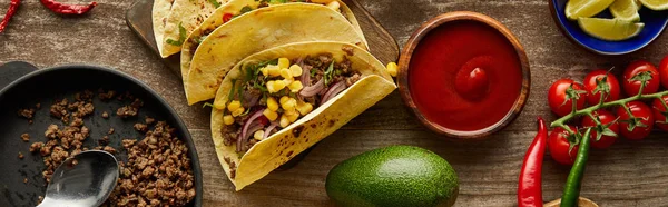 Vista superior de tacos tradicionales mexicanos con salsa de tomate e ingredientes en la superficie de madera, plano panorámico - foto de stock