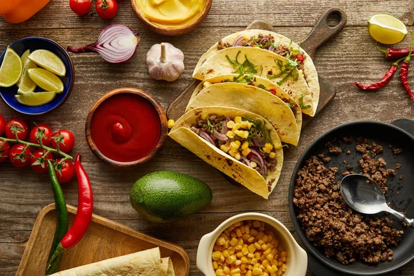 Draufsicht auf gekochte Tacos mit Gemüse und Soßen auf Holzoberfläche — Stockfoto