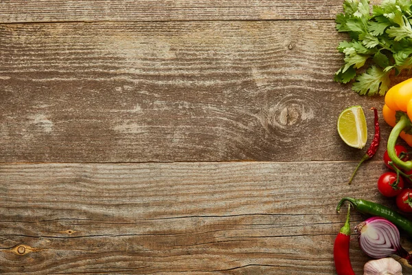 Vista superior de verduras crudas con rodajas de lima y vegetación sobre fondo de madera con espacio para copiar - foto de stock