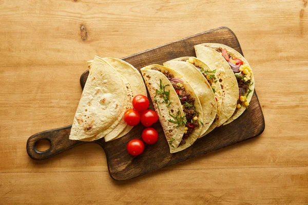 Vista dall'alto dei tradizionali tacos messicani con pomodorini ciliegini sul tagliere su superficie di legno — Foto stock