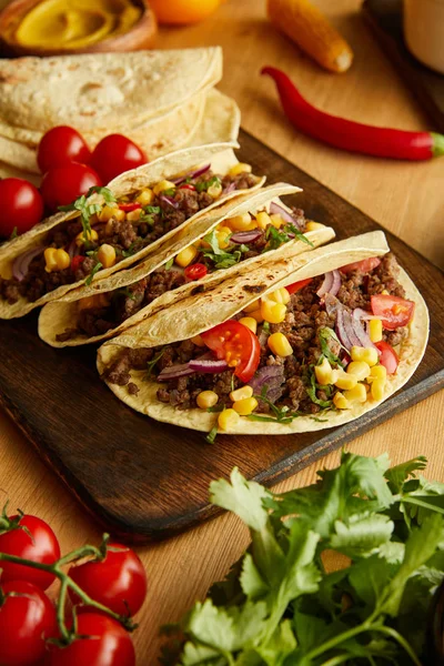 Delicious tacos with ripe vegetables and greenery on wooden table — Stock Photo