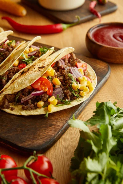 Sabrosos tacos sobre tabla de cortar con verduras frescas sobre fondo de madera - foto de stock