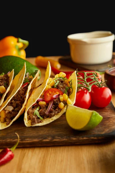 Leckere Tacos mit Limetten und Kirschtomaten auf Holztisch auf schwarzem Hintergrund — Stockfoto