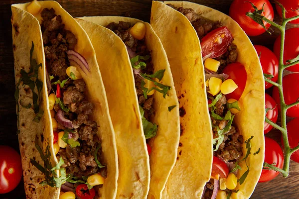 Draufsicht auf leckere Tacos mit reifen Kirschtomaten auf Holzgrund — Stockfoto