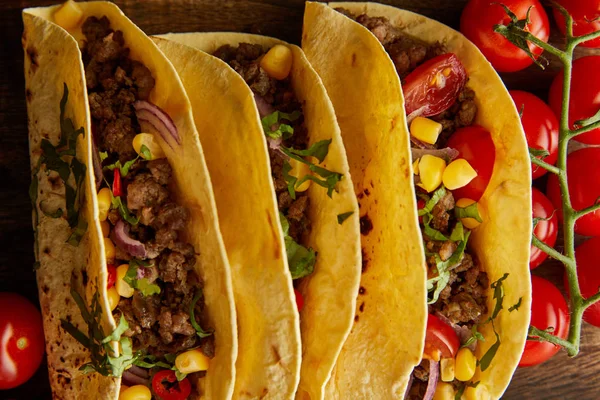 Vista superior de sabrosos tacos con tomates cherry maduros sobre fondo de madera - foto de stock