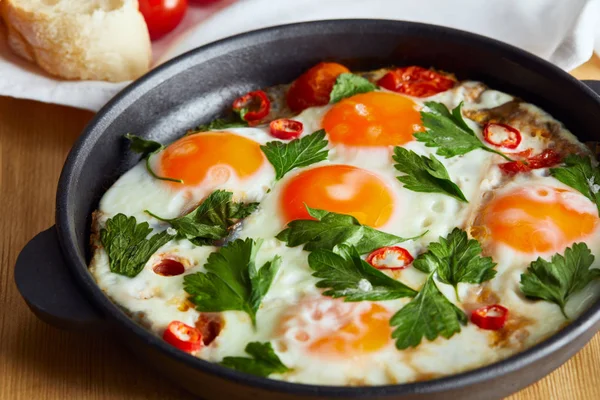 Cerrar vista de huevos fritos con perejil y chile en sartén sobre mesa de madera - foto de stock