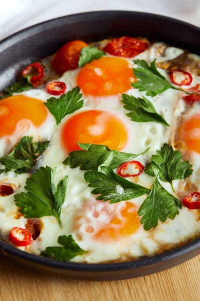 Close up view of fried eggs with parsley and chili pepper in pan on wooden table — Stock Photo