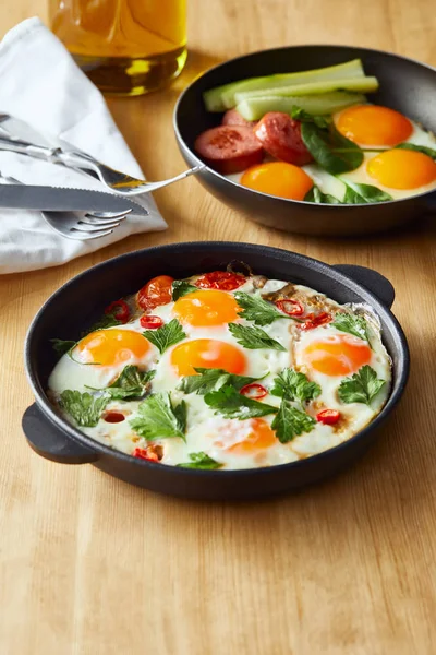 Selective focus of fried eggs in frying pans at wooden table with cutlery, napkin and oil — Stock Photo