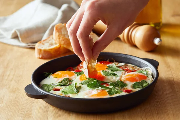 Cropped view of eating fried eggs with bread at wooden table — Stock Photo