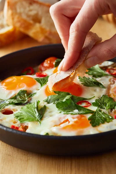 Cropped view of eating fried eggs with bread at wooden table — Stock Photo