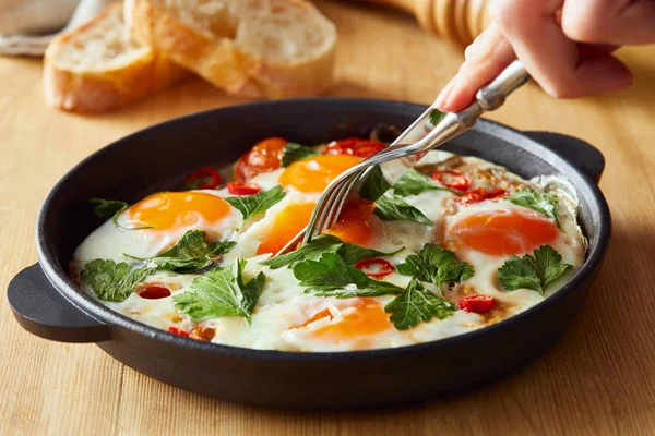 Cropped view of eating fried eggs with parsley and chili pepper on wooden table with fork and knife — Stock Photo