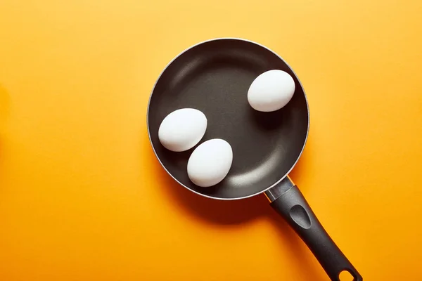 Top view of raw chicken eggs in frying pan on orange background — Stock Photo