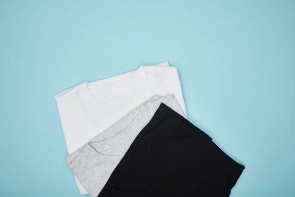 Vista superior de branco básico preto, branco e cinza camisetas isoladas em azul — Fotografia de Stock