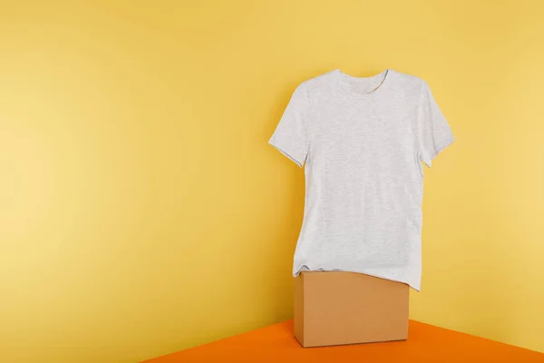 Basic grey t-shirt on cube on yellow background — Stock Photo