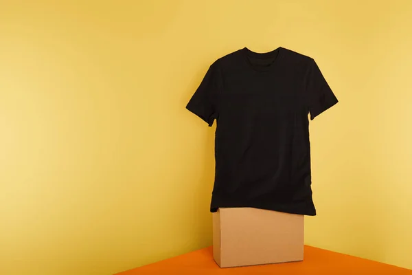 Basic black t-shirt on cube on yellow background — Stock Photo