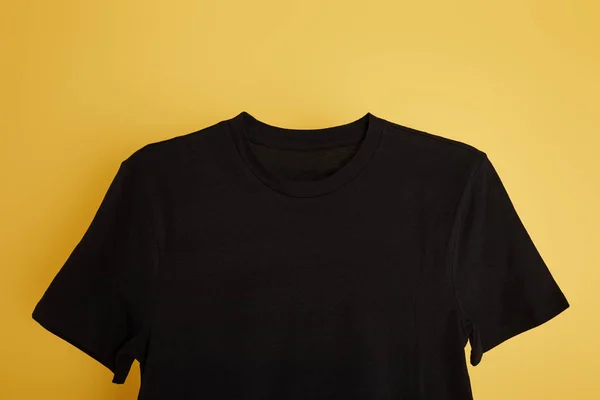 Vue du dessus du t-shirt noir basique sur fond jaune — Photo de stock