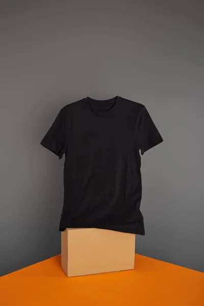 Basic black t-shirt on cube on grey and orange background — Stock Photo