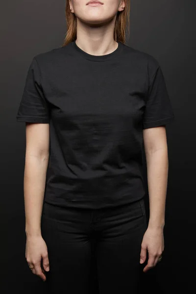 Ausgeschnittene Ansicht einer Frau im schwarzen T-Shirt auf schwarzem Hintergrund — Stockfoto