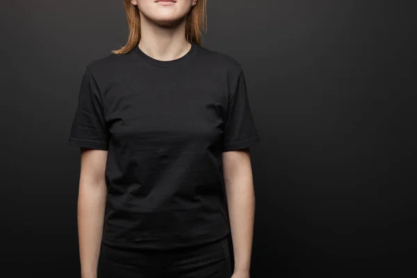 Corte vista de mulher em branco básico preto t-shirt no fundo preto — Fotografia de Stock