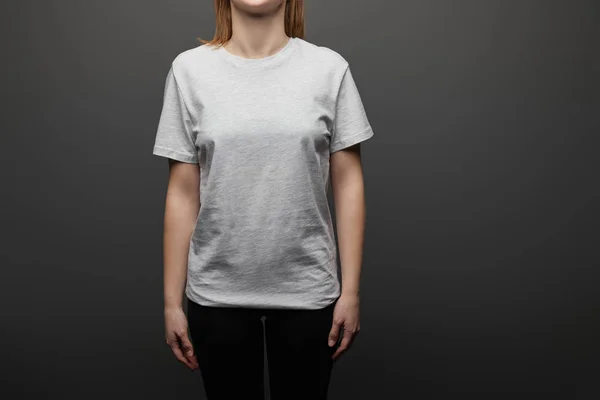 Cropped view of woman in blank basic grey t-shirt on black background — Stock Photo
