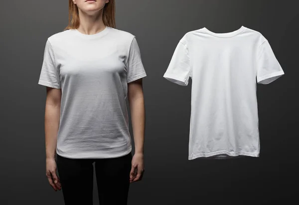 Cropped view of woman near blank basic white t-shirt on black background — Stock Photo