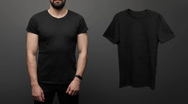 Cropped view of bearded man near blank basic black t-shirt on black background — Stock Photo