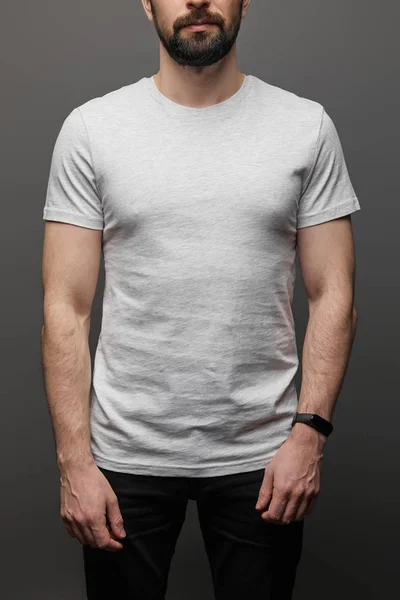 Vue recadrée de l'homme barbu en blanc t-shirt gris de base sur fond noir — Photo de stock