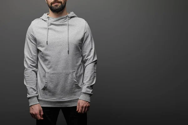 Cropped view of bearded man in blank basic grey hoodie on black background — Stock Photo