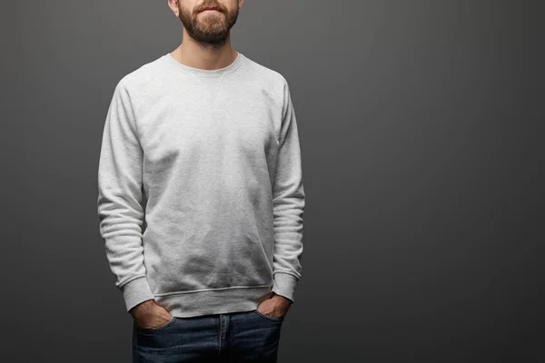 Обрізаний вид бородатого чоловіка з руками в кишенях в порожній базовий сірий светр на чорному фоні — стокове фото