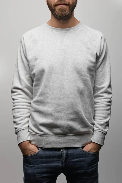 Partial view of bearded man in blank basic grey sweatshirt with hands in pockets isolated on grey — Stock Photo