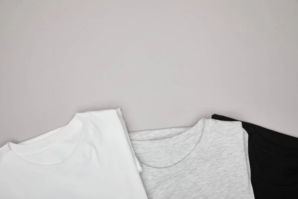 Top view of blank basic black, white and grey t-shirts isolated on grey — Stock Photo