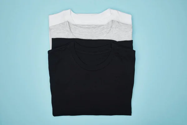 Top view of blank basic black, white and grey t-shirts isolated on blue — Stock Photo