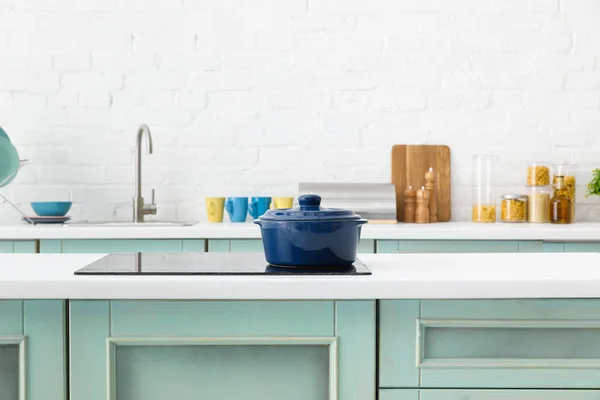 Selective focus of modern white and turquoise kitchen interior with pot on electric induction cooktop — Stock Photo