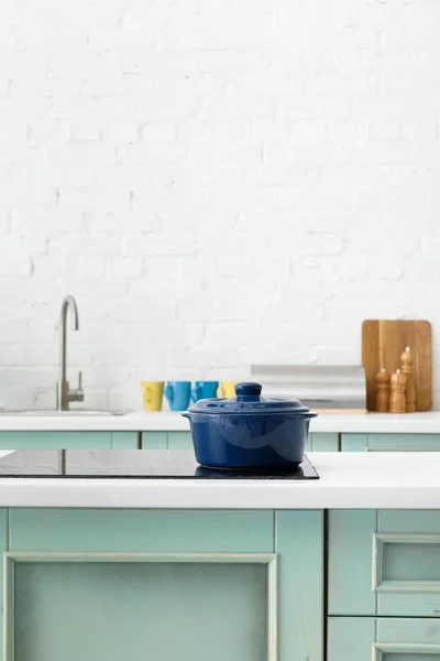 Selective focus of white and turquoise kitchen interior with pot on electric induction cooktop — Stock Photo