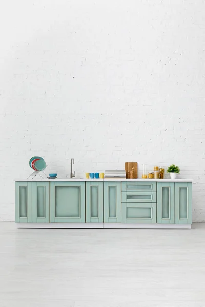 Modern white and turquoise kitchen interior with kitchenware near brick wall — Stock Photo