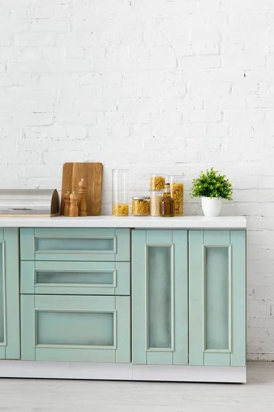 Intérieur moderne de cuisine blanche et turquoise avec ustensiles de cuisine, récipients pour aliments et plantes près du mur de briques — Photo de stock