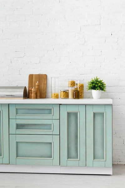 Moderno interior de cocina blanca y turquesa con utensilios de cocina, recipientes de alimentos y planta cerca de la pared de ladrillo - foto de stock