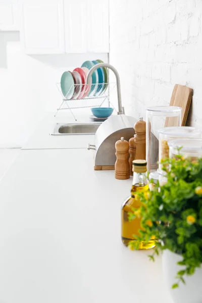 Selective focus modern white kitchen interior with kitchenware and green plant near brick wall — Stock Photo