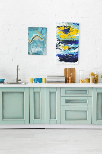 Modern white and turquoise kitchen interior with kitchenware and abstract paintings on brick wall — Stock Photo