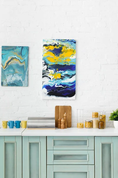 Moderne weiße und türkisfarbene Kücheneinrichtung mit Geschirr und abstrakten Gemälden an der Backsteinwand — Stockfoto