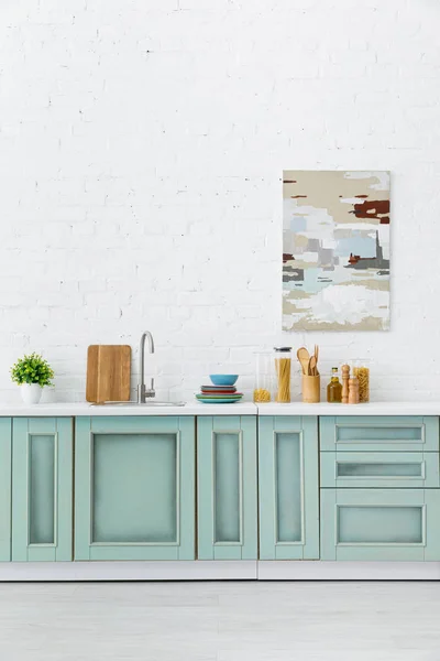 Intérieur de cuisine blanc et turquoise avec ustensiles de cuisine et peinture abstraite sur mur de briques — Photo de stock